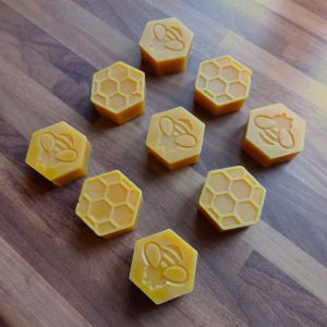 Hexagonin muotoisia mehiläisvahapalasia. Kuvassa yhdeksän palaa, joissa mehiläiskennokuviointi toisella puolella, mehiläisen kuva toisella.